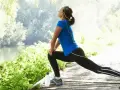 Donna fa stretching su un sentiero di legno vicino a un fiume, godendosi la natura e un buon rom articolare.