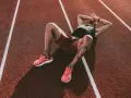 Atleta esausto a terra su una pista da corsa, mani sulla testa. Potrebbe essere il **significato di overtraining**: il corpo che chiede una pausa.