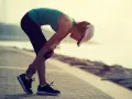 Donna con cappellino si piega tenendosi il ginocchio, forse a causa di un infortunio durante la corsa. La sua espressione suggerisce dolore, ma la sua determinazione è evidente. La scala di Borg potrebbe essere usata per valutare l'intensità dello sforzo.