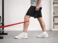 Uomo esegue esercizi per il vasto mediale obliquo con elastico rosso, rafforzando il ginocchio.