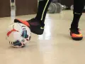 Un giocatore di calcio si prepara a calciare un pallone. Scarpe da calcio arancioni e nere, calzettoni neri con dettagli fluo.