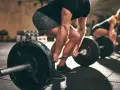 Uomo e donna si allenano in palestra con bilancieri. I suoi **doms bicipiti** sono visibili mentre solleva il peso.