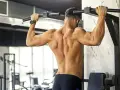Uomo con muscoli dorsali scolpiti che esegue trazioni alla sbarra in palestra.