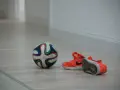 Pallone da futsal e scarpe arancioni su parquet. Pronto per una partita, ma cos'è il futsal? Uno sport veloce e tecnico.