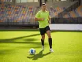 Giovane calciatore corre sul campo verde, allenando la resistenza. Un pallone da calcio è vicino a lui.