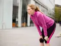 Donna bionda, esausta dopo la corsa, si piega appoggiando le mani sulle ginocchia. Il suo respiro affannoso indica un alto RPE (Rate of Perceived Exertion).