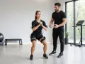 Donna in tuta EMS esegue squat con un trainer. Scopri i benefici dell'allenamento isometrico per un corpo tonico.