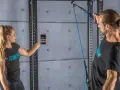 Donna con smartphone e uomo con cavo per allenamento. Il display mostra grafici, forse per misurare la forza o il progresso, spiegando cosa significa pr.