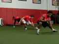 Giovani atleti in allenamento corsa calcio, eseguono esercizi di stretching e agilità su un campo sintetico.