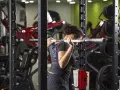 Donna esegue uno split squat con bilanciere nel multipower, concentrata sull'allenamento delle gambe.