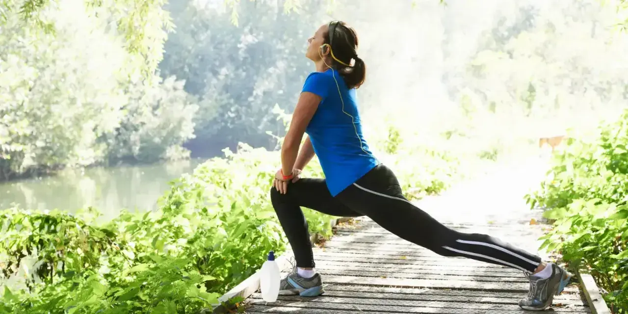 Donna fa stretching su un sentiero di legno vicino a un fiume, godendosi la natura e un buon rom articolare.