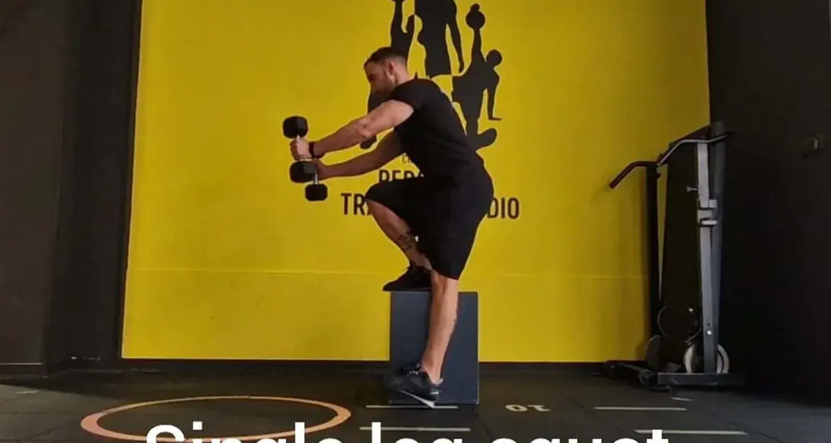 Uomo esegue squat monopodalico con manubri, allenamento per la forza e l'equilibrio.