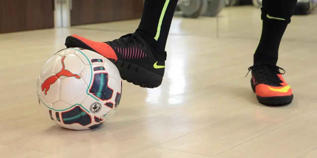 Un giocatore di calcio si prepara a calciare un pallone. Scarpe da calcio arancioni e nere, calzettoni neri con dettagli fluo.