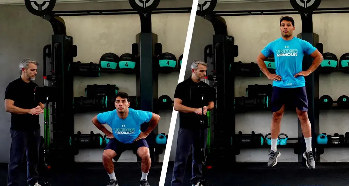 Uomo esegue un countermovement jump in palestra, guidato da un istruttore.