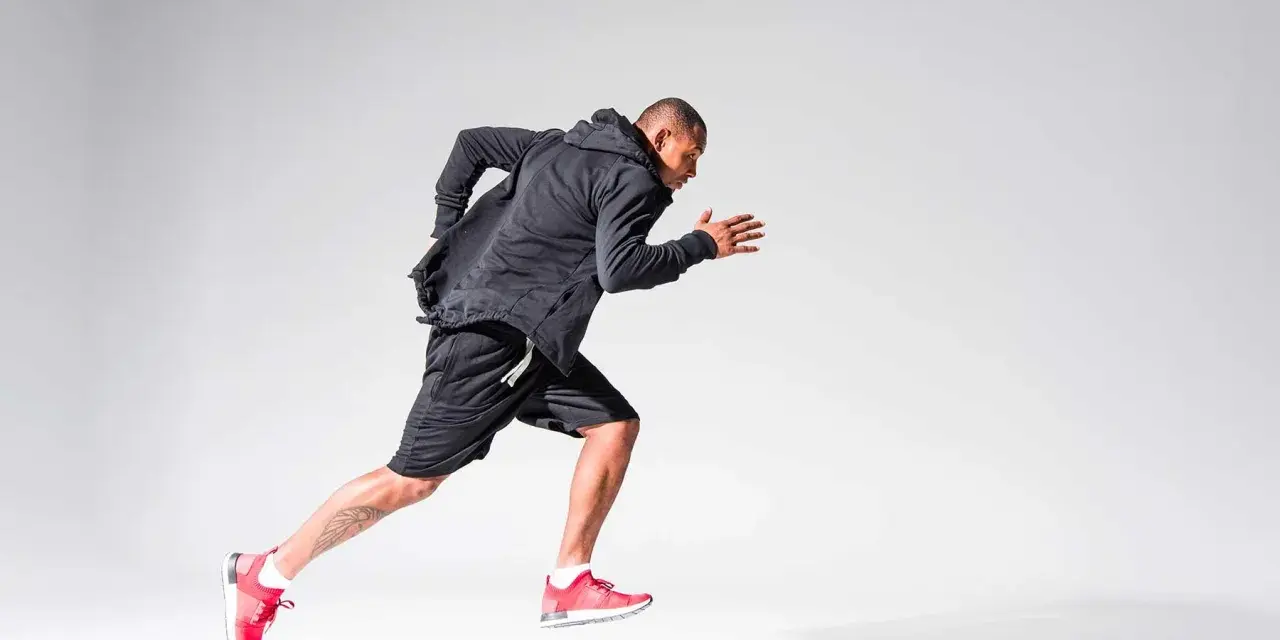 Atleta in corsa, concentrato sul suo obiettivo di aumentare il VO2max. Indossa abbigliamento sportivo nero e scarpe rosse.