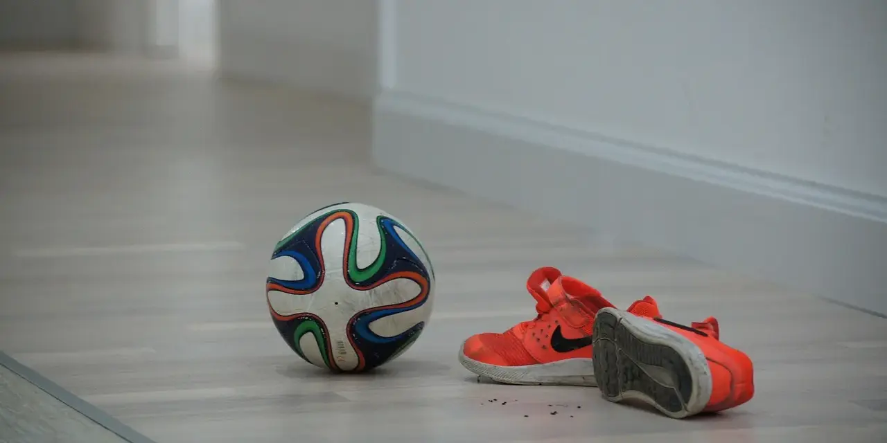 Pallone da futsal e scarpe arancioni su parquet. Pronto per una partita, ma cos'è il futsal? Uno sport veloce e tecnico.