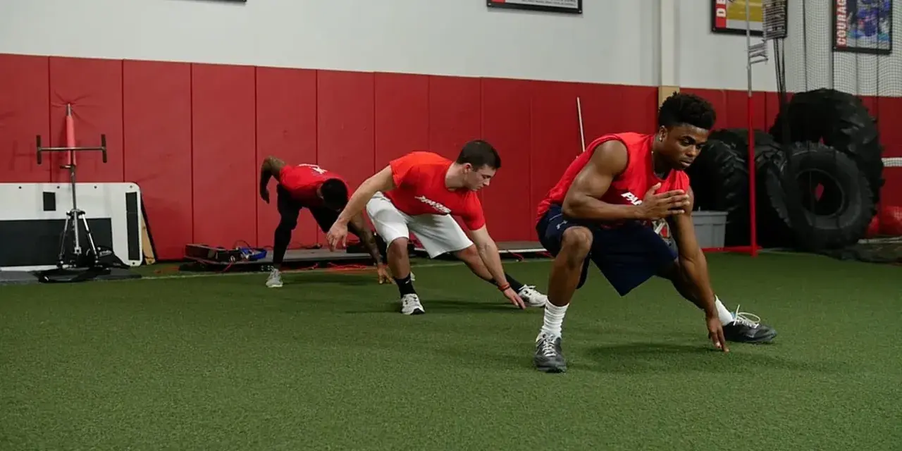 Giovani atleti in allenamento corsa calcio, eseguono esercizi di stretching e agilità su un campo sintetico.