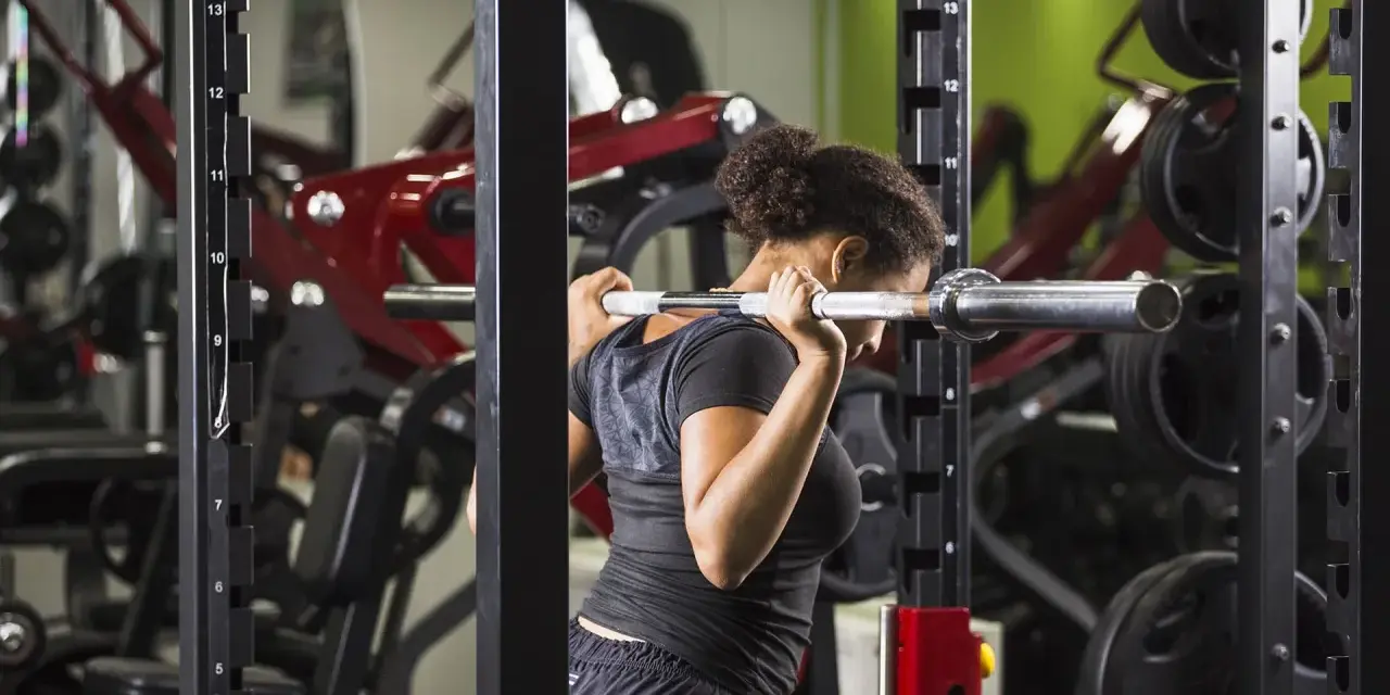 Donna esegue uno split squat con bilanciere nel multipower, concentrata sull'allenamento delle gambe.