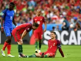 Un giocatore portoghese a terra, forse per un infortunio calcio, mentre un compagno si china preoccupato e un avversario osserva.