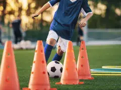 Giovane calciatore si allena con esercizi rapidità calcio senza palla, slalom tra i coni arancioni su un campo verde.