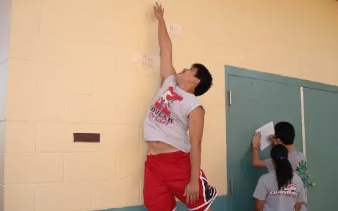 Ragazzo esegue un sargent test, allungandosi verso un segno sul muro. Altri ragazzi registrano i risultati.