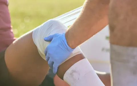 Medico con guanto blu fascia la gamba di un atleta, probabilmente per una lesione adduttore.