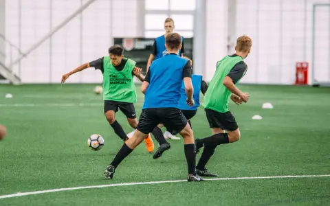 Giovani calciatori in allenamento, con pettorine verdi e blu, corrono su un campo sintetico. L'intensità dell'allenamento richiede un **aerobico alto**.