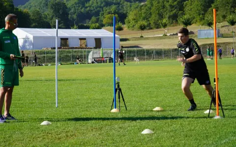 Allenatore osserva un atleta eseguire un test di agilità, con coni e paletti disposti sul campo per il **yoyo test tabella**.