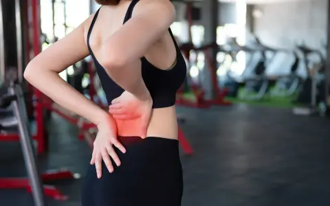 Donna in palestra con le mani sulla schiena, evidenziando il **dolore schiena bassa**.