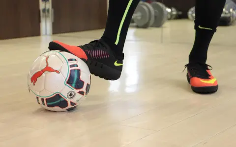 Un giocatore di calcio si prepara a calciare un pallone. Scarpe da calcio arancioni e nere, calzettoni neri con dettagli fluo.