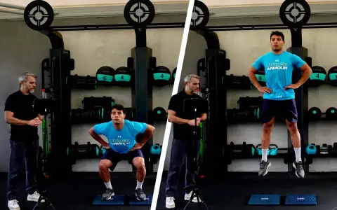 Uomo esegue un countermovement jump in palestra, guidato da un istruttore.
