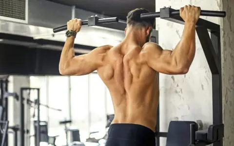 Uomo con muscoli dorsali scolpiti che esegue trazioni alla sbarra in palestra.