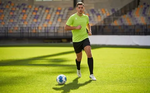 Giovane calciatore corre sul campo verde, allenando la resistenza. Un pallone da calcio è vicino a lui.