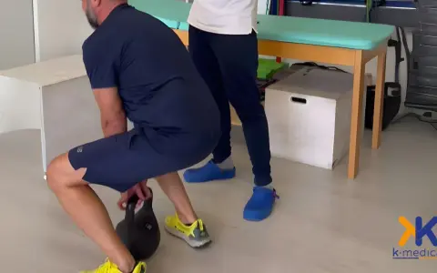 Uomo in riabilitazione per tendinite adduttori esegue squat con kettlebell, assistito da un terapista.
