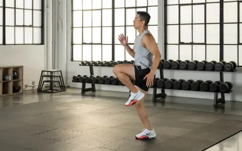 Uomo in palestra esegue un esercizio per i muscoli polpaccio, con manubri sullo sfondo.