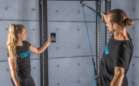 Donna con smartphone e uomo con cavo per allenamento. Il display mostra grafici, forse per misurare la forza o il progresso, spiegando cosa significa pr.