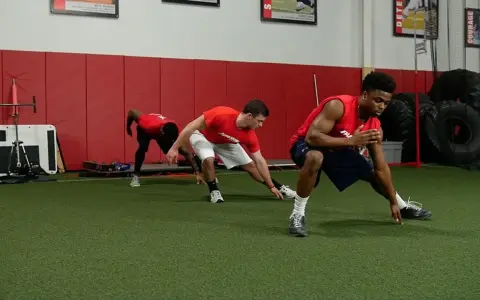 Giovani atleti in allenamento corsa calcio, eseguono esercizi di stretching e agilità su un campo sintetico.