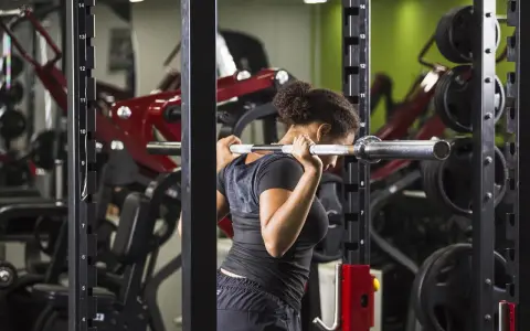 Donna esegue uno split squat con bilanciere nel multipower, concentrata sull'allenamento delle gambe.