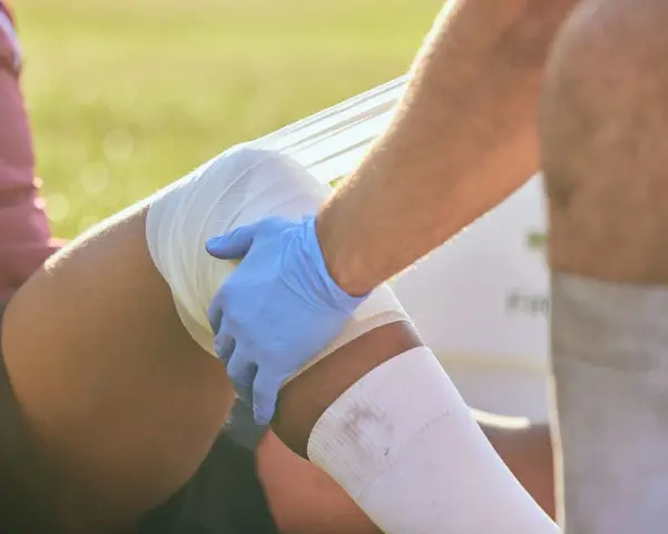 Medico con guanto blu fascia la gamba di un atleta, probabilmente per una lesione adduttore.