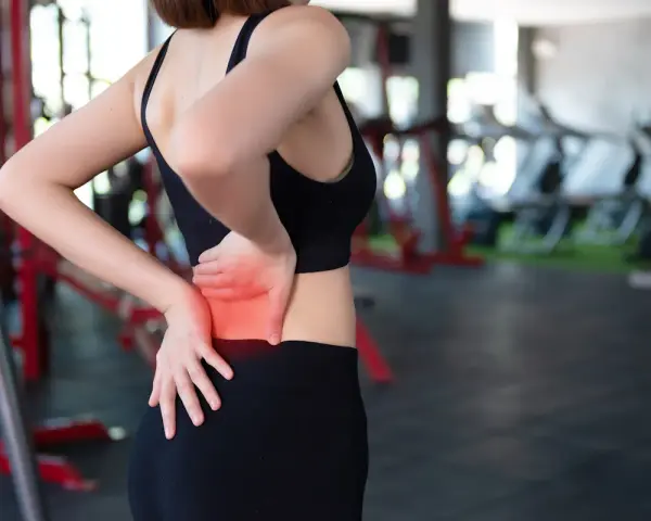 Donna in palestra con le mani sulla schiena, evidenziando il **dolore schiena bassa**.