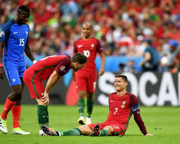 Un giocatore portoghese a terra, forse per un infortunio calcio, mentre un compagno si china preoccupato e un avversario osserva.