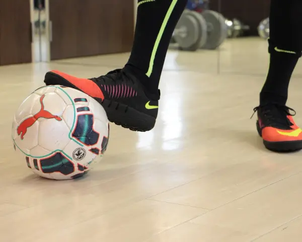 Un giocatore di calcio si prepara a calciare un pallone. Scarpe da calcio arancioni e nere, calzettoni neri con dettagli fluo.