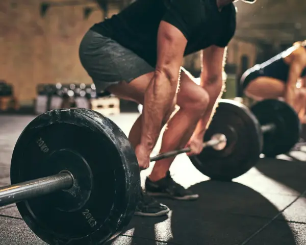 Uomo e donna si allenano in palestra con bilancieri. I suoi **doms bicipiti** sono visibili mentre solleva il peso.