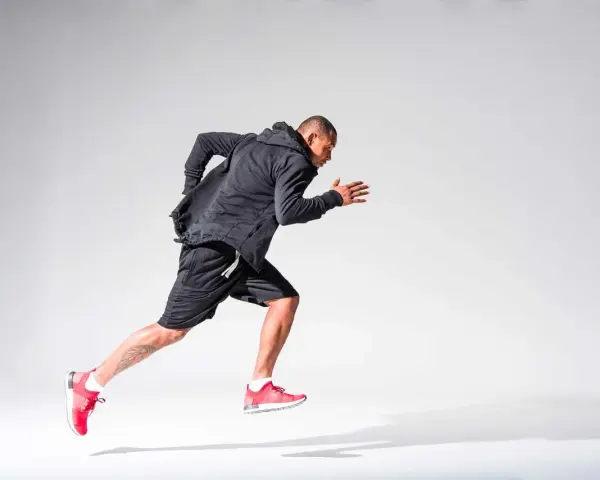 Atleta in corsa, concentrato sul suo obiettivo di aumentare il VO2max. Indossa abbigliamento sportivo nero e scarpe rosse.