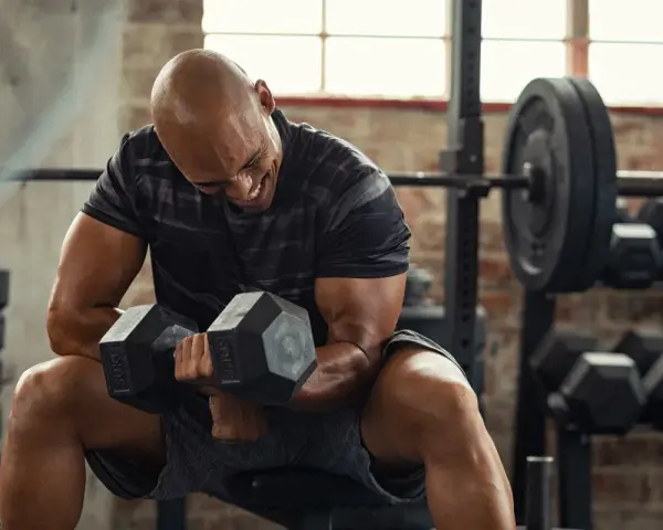Uomo calvo in palestra, concentrato su un curl con manubri da 50 kg. Il suo viso mostra lo sforzo, indicando un RPE chart elevato.