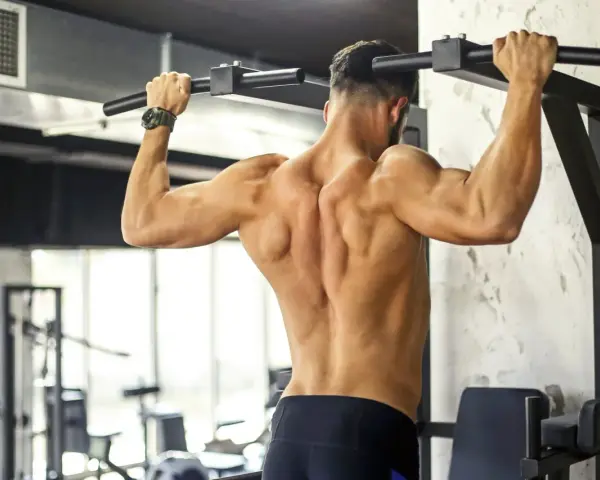 Uomo con muscoli dorsali scolpiti che esegue trazioni alla sbarra in palestra.