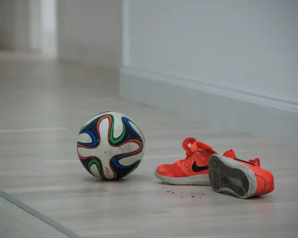 Pallone da futsal e scarpe arancioni su parquet. Pronto per una partita, ma cos'è il futsal? Uno sport veloce e tecnico.