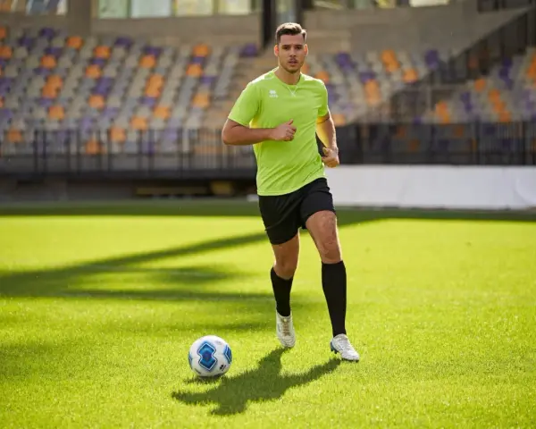 Giovane calciatore corre sul campo verde, allenando la resistenza. Un pallone da calcio è vicino a lui.