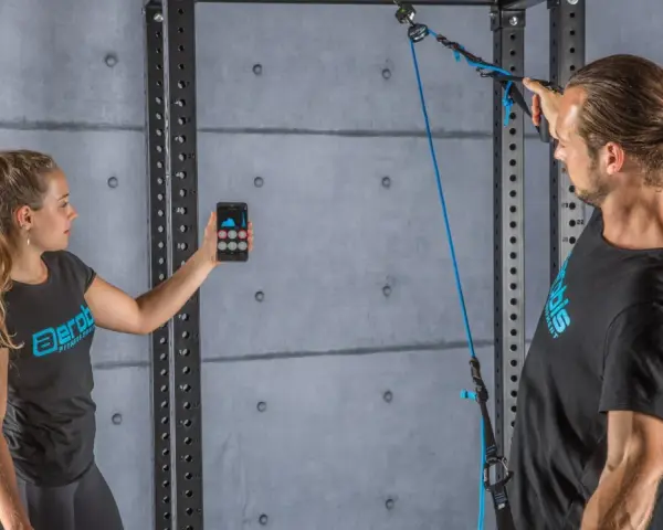 Donna con smartphone e uomo con cavo per allenamento. Il display mostra grafici, forse per misurare la forza o il progresso, spiegando cosa significa pr.