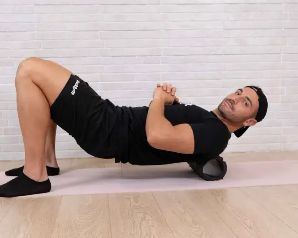 Uomo con foam roller sotto la schiena, mostrando cosa succede ai muscoli dopo l'allenamento. Recupero muscolare.